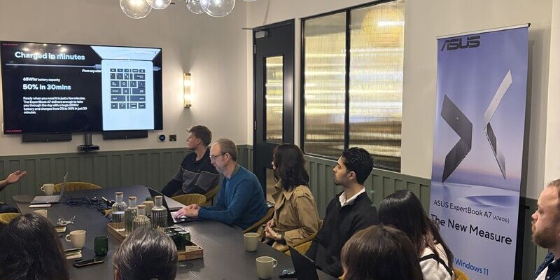 Journalists gathered around a table at an ASUS ExpertBook media briefing, with a presentation screen and ASUS banner.