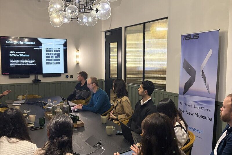 Journalists gathered around a table at an ASUS ExpertBook media briefing, with a presentation screen and ASUS banner.